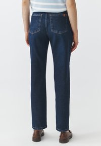 Temno modri jeans s ravnim krojem, ki imajo dve zadnji žep in majhno usnjeno oznako na desnem žepu.