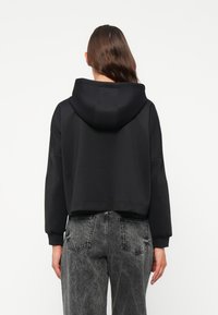 Svart cropped hettegenser med teksturert finish, med hette og lange ermer. Kombinert med høytaljede, grå slitte denimjeans.