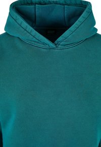 Tīrkīza krāsa kapuce ar mīkstu audumu, ar plašu kakla atvērumu un divslāņu kapuci. Gluda tekstūra bez redzamām rakstu daļām.