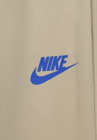 Bežna tkanina z teksturirano površino, ki ima izstopajoč modr Nike logo in znak swoosh v spodnjem desnem kotu.