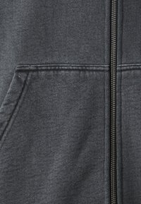 Felpa con zip grigia scura realizzata in tessuto morbido. Presenta una zip liscia, due tasche frontali e polsini e orlo a costine. La texture appare leggermente mélangé.