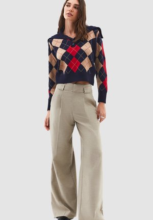 Navy blue cropped sweater with argyle pattern in beige and red, featuring a hood and buttons. Paired with high-waisted light gray wide-leg trousers.