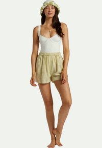 Fehér pamut ujjatlan felső, amelyet világos sárga és fehér csíkos rövidnadrággal párosítottak. Az öltözet laza szabással és rugalmas derékbőséggel rendelkezik.