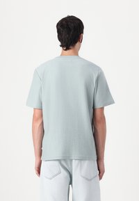 Light blue short-sleeve t-shirt with a textured fabric, round neck, and relaxed fit. Paired with light denim pants.