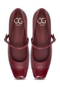 Punaiset nahka-ballet-kengät, joissa on kiiltävä patenttinen kärki ja nilkkahihna. Ominaisuuksia ovat pyöreä muoto ja sileä pinta, sisäpuolella kohokuvioitu logo.