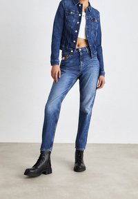 Tmavě modrá džínová bunda, zkrácený střih s knoflíky a kapsami. Světlé modré rovné džíny, doplněné černými šněrovacími kotníkovými botami.