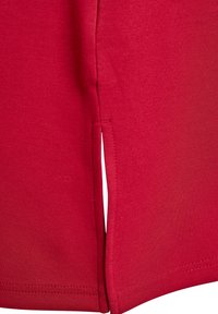 Červený bavlnený odev s bočnými rozparky, hladká textúra a čisté švy. Má priliehavý strih s jednoduchým, moderným vzhľadom.