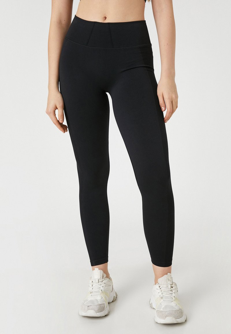 Svarta leggings med hög midja och åtsittande design, tillverkade av stretchigt material, i kombination med vita och grå träningsskor.