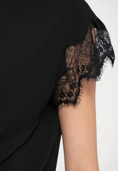 Čierny top s čipkovým lemom na rukávoch, ktorý vystavuje jemnú textúru a plynulý dizajn s ošúchanými hranami.
