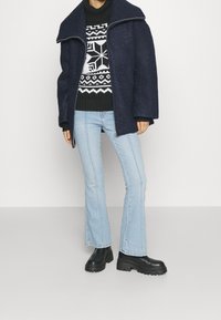 Marinblå ullblandad kappa med överdimensionerad krage, svartvit mönstrad tröja, ljusblå utsvängda jeans och svarta kraftiga klackstövlar.