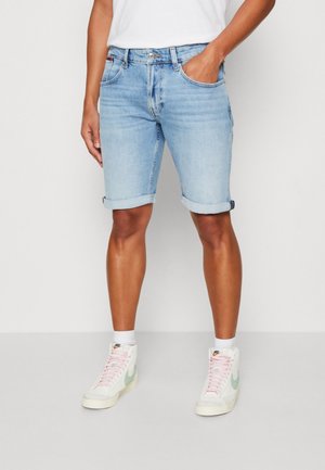 Shorts en jean bleu clair avec ourlet retroussé, design à cinq poches et légère décoloration. Associés à des baskets blanches avec un accent menthe.