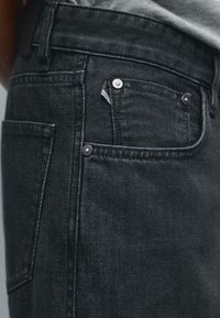 I jeans in denim nero presentano un classico design a cinque tasche, una texture morbida e cuciture sottili, con bottoni in metallo argentato e un dettaglio sulla tasca minore.