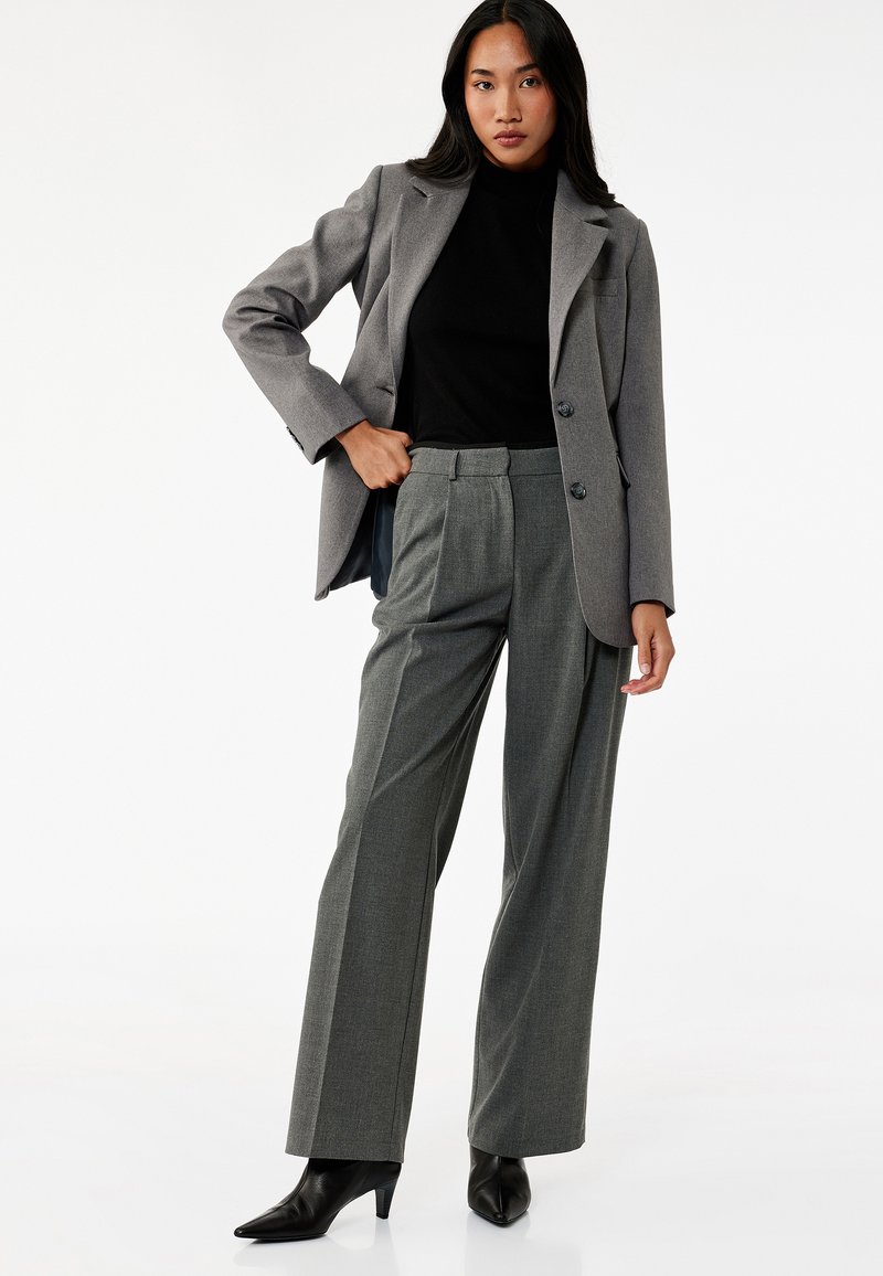 Szary żakiet z dwoma guzikami, czarna bluzka z wysokim kołnierzem i szare szerokie spodnie. Skórzane botki na obcasie z szpiczastym noskiem. Gładka faktura, dopasowany krój.