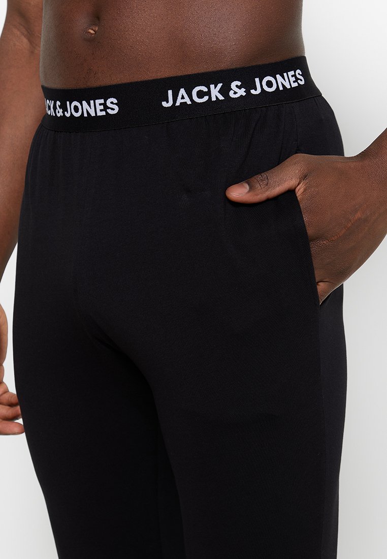 Pantalones de lounge negros con cintura elástica que presentan el logo "JACK & JONES" en blanco. La tela parece suave y tiene un ajuste relajado.