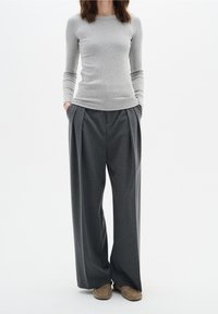 Grå långärmad ribbad topp i kombination med högmidjade, löst sittande, mörkgrå plisserade byxor. Byxorna har sidofickor. Avslappnat fotarbete.