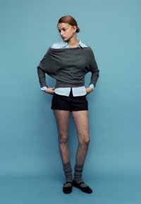 Siv prevelik pulover z modro črtasto srajco pod njim, črni kratki hlači, vzorčaste nogavice in sive nogavice do kolen s črnimi čevlji.