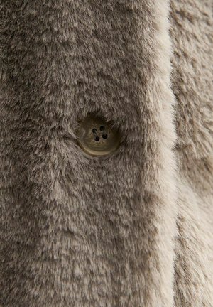 Nep bontstof in licht taupe met een zachte, gestructureerde oppervlakte; bevat een heldere knoop met vier gaten, geplaatst aan de linkerkant.