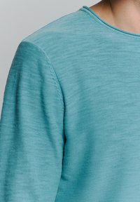 Lichtblauwe trui met een ronde hals, textuurstof en subtiele stikdetails langs de schoudernaden.
