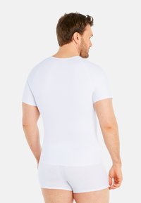 White short-sleeve shirt made of stretchy fabric, fitted design, and smooth texture. Short white trunks with a similar material.