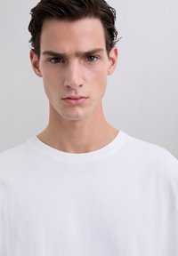 Camiseta de algodón blanca con cuello redondo y mangas cortas, que presenta una textura suave y un diseño simple sin patrones ni adornos.