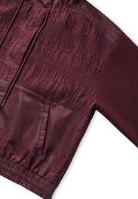 Chaqueta de sudadera granate con una sección superior texturizada, una sección inferior lisa y dobladillo elástico. Cuenta con un bolsillo frontal y capucha con cordón.