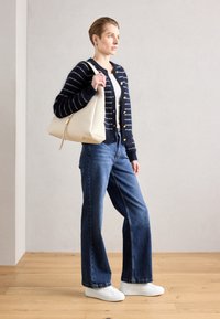 Marine gestreifter Cardigan mit goldenen Knöpfen, weißem Oberteil, blauen weiten Jeans und weißen Turnschuhen. Trägt eine beigefarbene, lässige Handtasche.