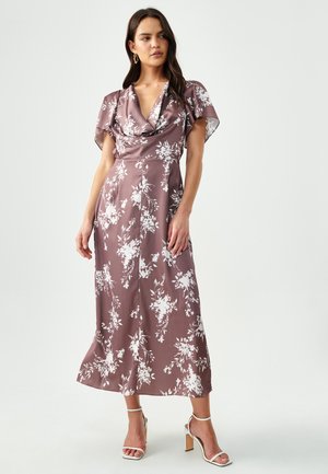 Sleeveless, cowl-neck dress in soft mauve fabric with white floral pattern. Flowy silhouette extends to mid-calf, worn with white heeled sandals.