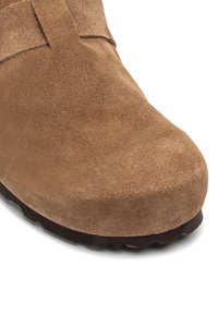 Bruine suède schoen met een ronde neus en een dikke rubberen zool. De bovenkant heeft een gladde textuur en minimale stikdetails.
