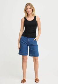Canotta nera senza maniche abbinata a pantaloni corti in denim blu di lunghezza media con tasche laterali e orlo risvoltato. Sandali piatti marroni completano l'outfit.