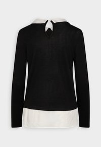 Haut noir à manches longues avec une sous-couche blanche à col et un détail en trou de serrure au dos, présentant une texture douce et des couleurs contrastées.