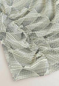 Tissu à motifs en noir et blanc avec des formes géométriques. Tissage texturé avec des lignes alternées et des motifs à carreaux, créant une profondeur visuelle.