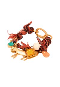 Pulsera de tono dorado con una banda de tela roja estampada, un charm con forma de perro y detalles de piedras preciosas coloridas.