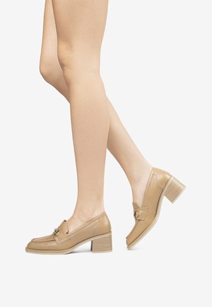 Beige Lederloafer mit kleinem Blockabsatz, ausgestattet mit einer dekorativen Schnalle und gestickten Details auf dem Obermaterial. Glatte Textur.