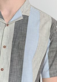 Korte mouw knoopshirt met contrasterende strepen in grijs, lichtblauw en crème, van een textuurstof met houten knopen.