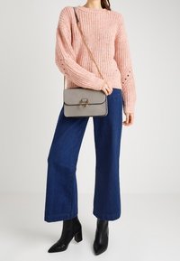 Różowy sweter dziany o prążkowanej fakturze, zestawiony z szerokimi niebieskimi jeansami i czarnymi botkami na obcasie. Szara torebka na łańcuszkowym pasku.