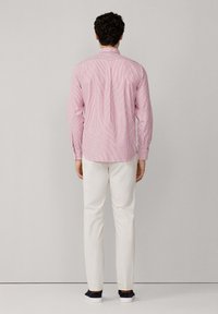 Camisa de manga larga a rayas rojas y blancas con cuello, combinada con pantalones blancos y zapatillas oscuras, mostrando un ajuste relajado y un diseño en la parte posterior.