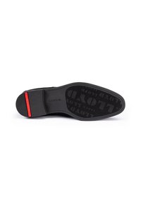 Suela de zapato de vestir negro con el texto grabado "LLOYD", que presenta un acento rojo en el tacón, aislada sobre un fondo blanco.