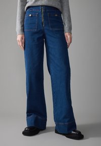 Denim wide-leg pants in deep blue, featuring a gold zipper and button accents, with large back pockets and a straight cut at the hem.