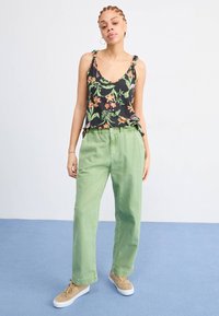 Top sans manches noir à motifs floraux verts et oranges, associé à un pantalon léger vert clair à coupe ample et des baskets beiges avec semelles blanches.