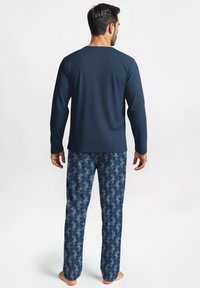 Marineblauwe longsleeve top met een ronde halslijn, gecombineerd met blauwe pyjamabroek met een koraalachtig patroon in lichter blauw. Glad stoffenafwerking.