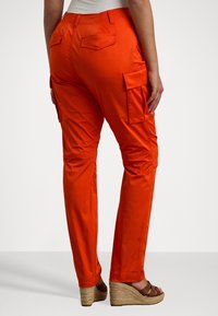 Orange cargobyxor med slim fit, utrustade med två sidofickor och två bakfickor, tillverkade av ett mjukt och lätt tyg.