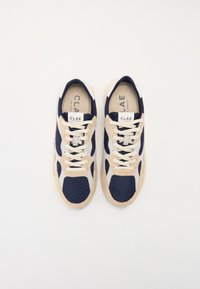 Navy mesh and beige suede sneakers with white laces and branding on the tongue; rounded shape with textured accents on the sides.