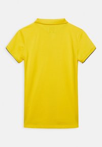 Žluté polo tričko s krátkými rukávy, s klasickým límcem a kontrastním tmavým lemováním kolem okrajů rukávů. Hladká bavlněná textilie.