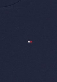 Granatowa bawełniana koszulka z małym haftowanym logo w białym, czerwonym i niebieskim kolorze, z okrągłym dekoltem i gładką teksturą.