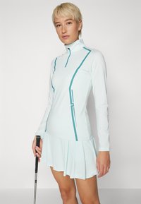 Light blue golf dress with long sleeves, half-zip collar, and teal accent lines. Features a pleated skirt with a smooth texture.