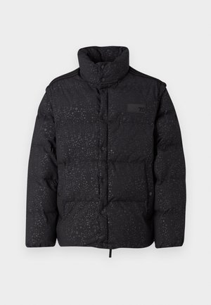 Mustan värvi pusterkate, millel on kõrge kaelus, nööpkaelus ja tekstureeritud pind. Seljas musta topi peal, helesinised teksad ja valged tosud.