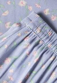 Helllila Stoff mit kleinen weißen und rosa Blumen und grünen Stängeln, der mit geraffter elastischer Naht auf einem Kleidungsstück versehen ist.