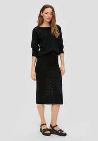 Zwart gebreid top en rok set met een chevronpatroon. De top heeft een relaxte pasvorm en de rok is aansluitend met een midi-lengte. Zwarte sandalen.