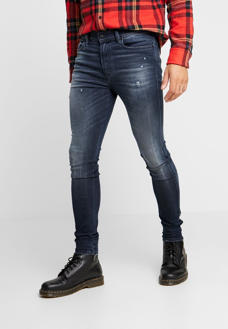 Blå skinny jeans med urblekta sektioner och lätt slitna detaljer, kombinerade med svarta snörboots. Tillverkade av jeansmaterial.
