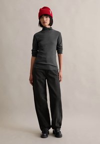 Grå långärmad topp med hög krage, kombinerad med vida svarta byxor och svarta skor, kompletterad med en röd stickad mössa.